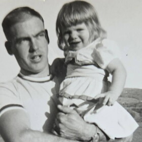 Black and white photo of smiling young girl in a white dress, held by young man looking pensive