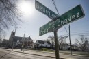 Outdoor photo of a city street with a church and homes in the background. In foreground is a street sign that reads "Avenida Cesar E. Chavez" on one sign "Belleview" on the other.