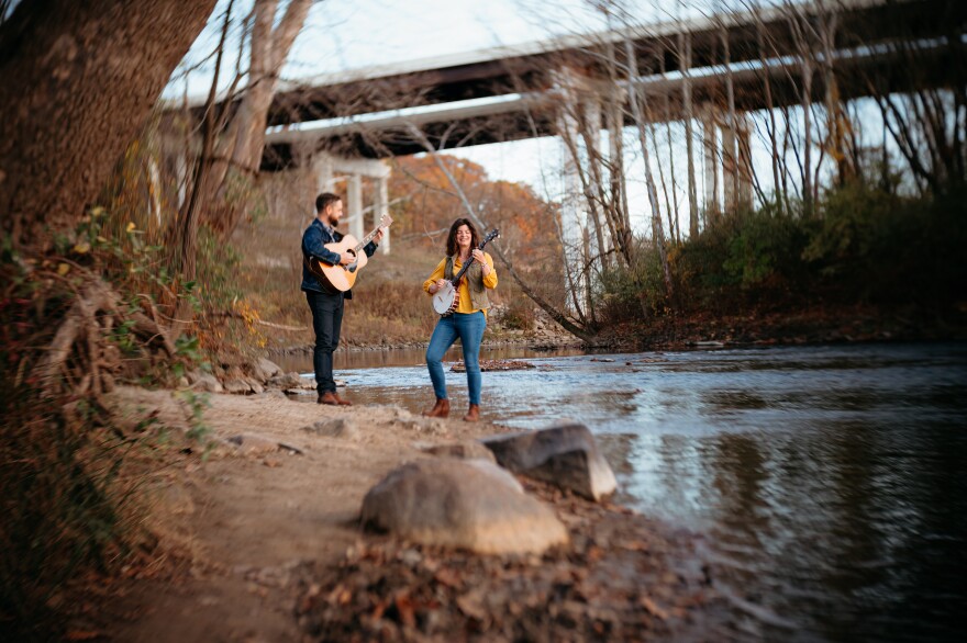 Craig Mast and Aubrey Helmuth Miller hold acoustic instruments near a body of water outside
