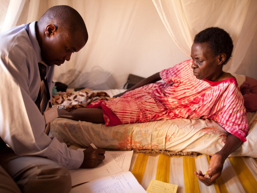 An HIV-positive woman, living alone in a one-room house, speaks with a visiting doctor.