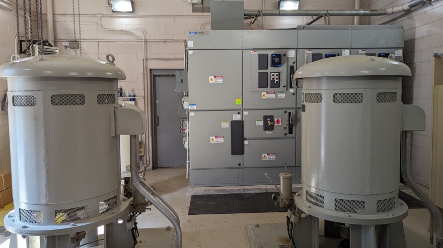 Two metal cylinders stand before a control panel inside a cinderblock building.