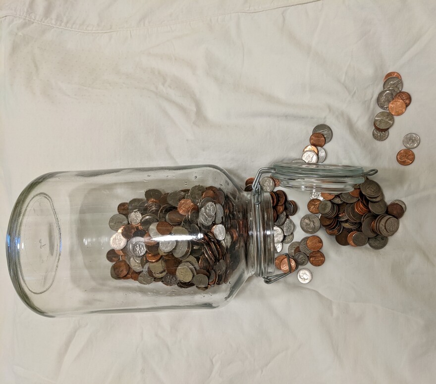 A glass jar with coins spilling out of it from the right.