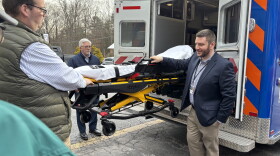 Delaware Township Ambulance Corps shows their new automated stretcher to local politicians. The stretcher allows for better control of patients' positions, and reduces the risk of back injury for EMS workers. Corps President Carl Will and EMS Chief Kyle Wright move the stretcher. Pike County Chairman Matthew Osterburg watches from afar.