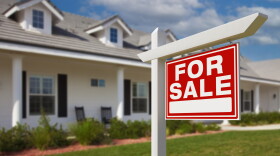 A white apartment buildings with a red sign in front of it that says "For Sale". 