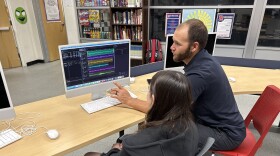 A high school student and teacher are sitting in front of a computer and editing an audio file.
