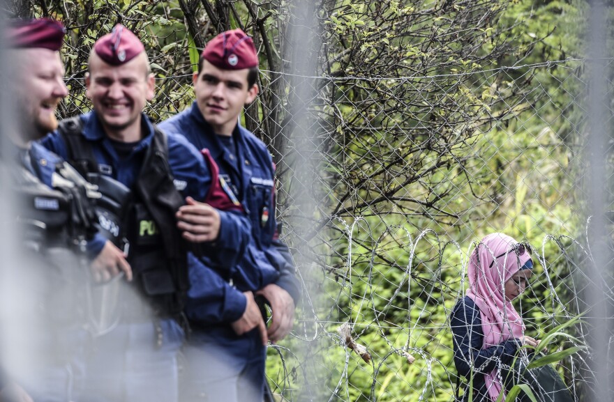 Hungarian border police talk next to a fence, next to a woman who is among hundreds of refugees and migrants caught behind a fence at the Hungarian border with Serbia Wednesday.