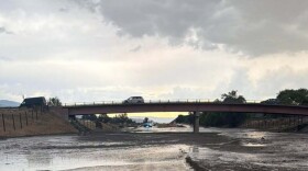 Water and mud covering a closed highway with a car on a bridge above it.