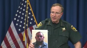 Polk Sheriff Grady Judd holds a mug shot of Deputy Peter Heneen
