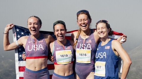 Four women in USA-themed running outfits and sneakers pose at the top of a mountain, with an American flag behind them.
