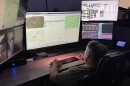 An emergency dispatcher sits in front of a bank of screens with maps and other information displayed.