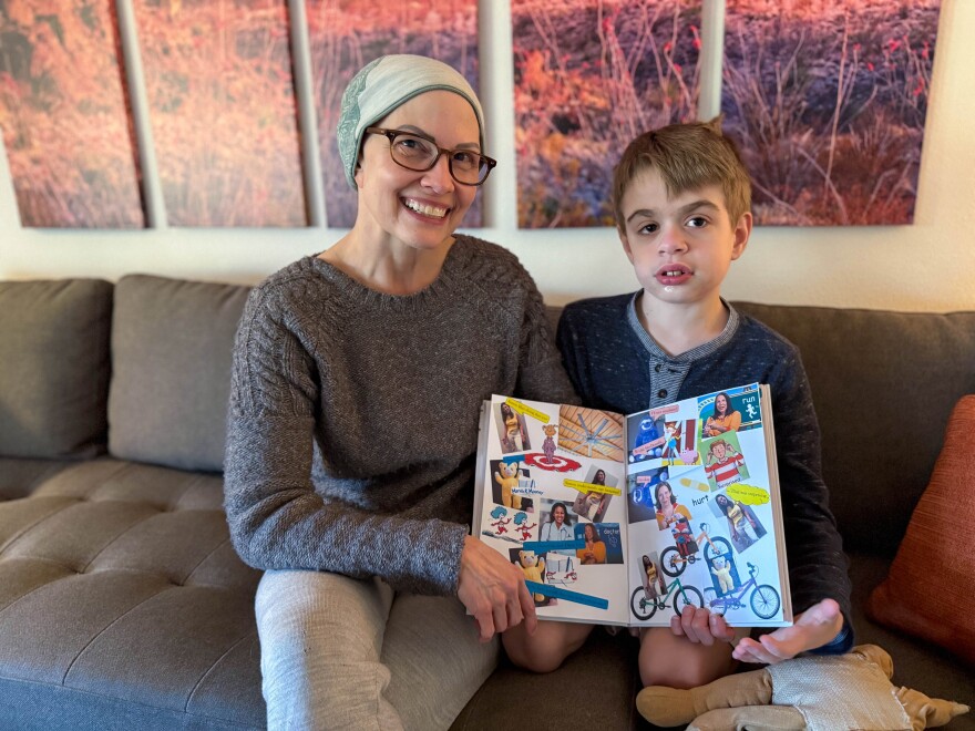 A woman sits on the couch with her son holding a picture book they created. 