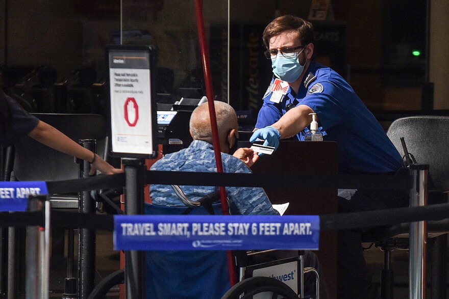 A man using a wheelchair hands his ID to an officer at a security screening checkpoint at Orlando International Airport in 2020.