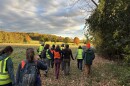 A group of people in high-visibility vests travel along the edge of a forest 