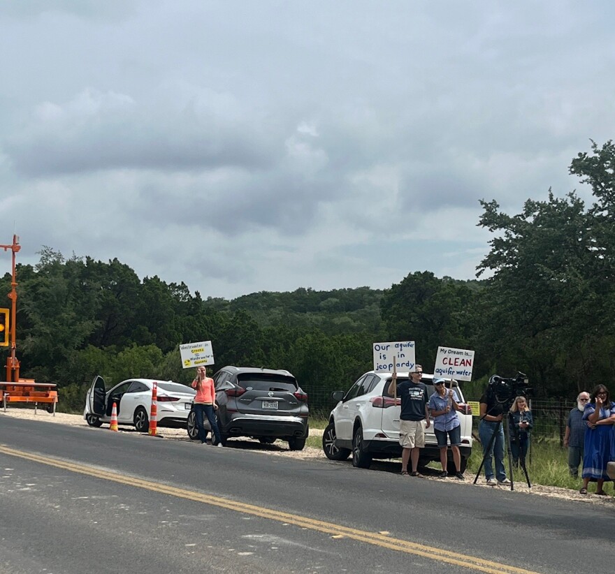 Protestors hold up signs as workers begin cutting trees for a water line in NW Bexar Country