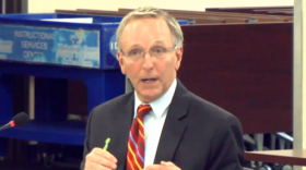 A man with glasses centered in frame with a suit and a red tie with multicolored stripes