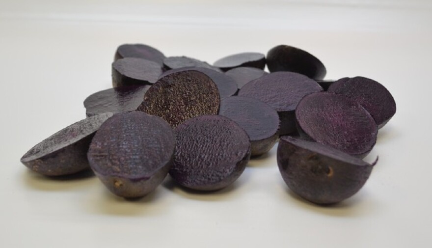 A professional image of dark purple potatoes sliced in half on a white background. 