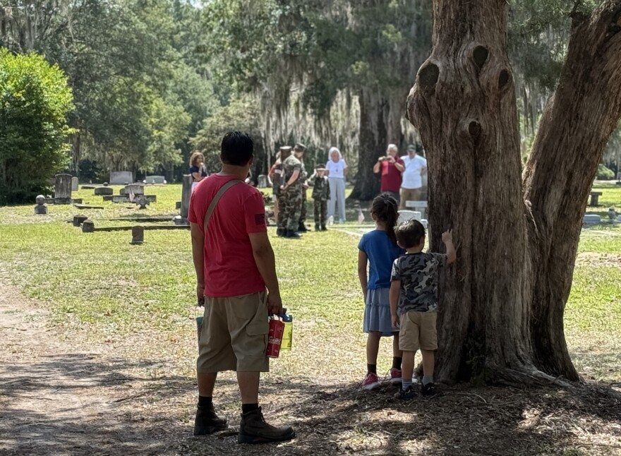 Alexander Santos (left) and his children Riley and Logan watch and wait as the Milton Lewis Young Marines pay service on Memorial Day to their namesake, Milton Lewis, the first Alachua County casualty of World War II. (Henry DeAngelis/WUFT News)