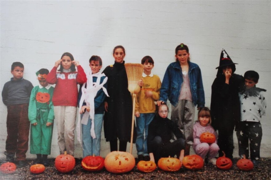 A group of children in costumes stand in front of carved pumpkins at Halloween time.