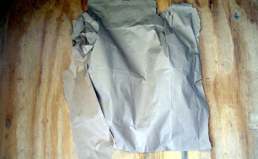 A brown paper bag showing contours is attached to the wood with staples. 