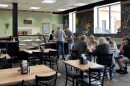 Patrons sit at tables and order food at a cafe and coffee shop.