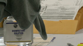 A stack of mail-in ballots to be sent out to voters, with a bottle of sanitizer nearby.