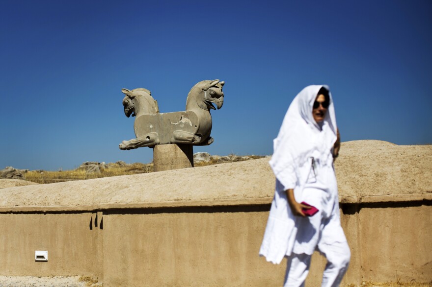 A foreign tourist at Persepolis walks past a statue of a double griffin, a mythical animal with the body of a lion and head and wings of an eagle.