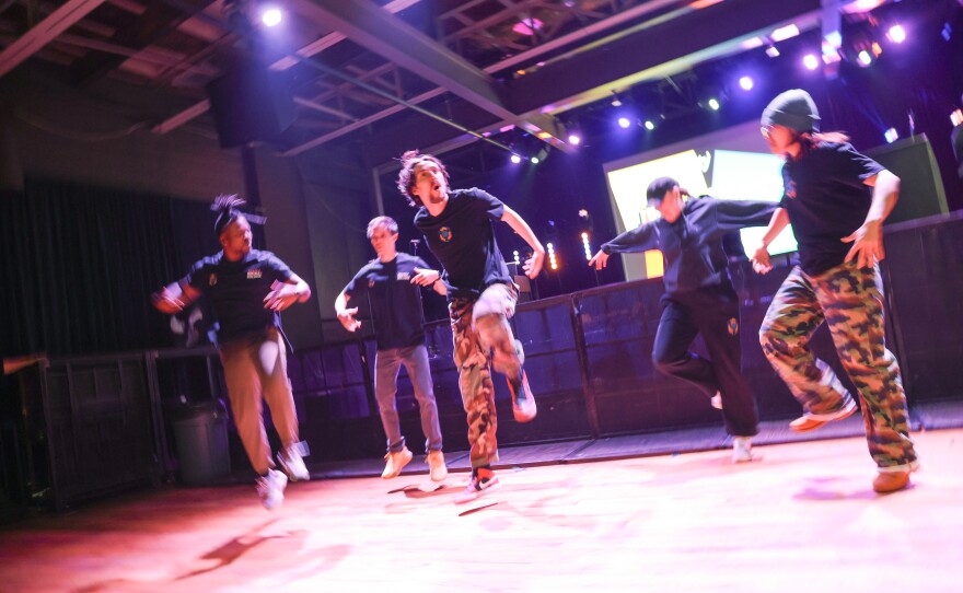 Several young men enthusiastically dance on a stage.