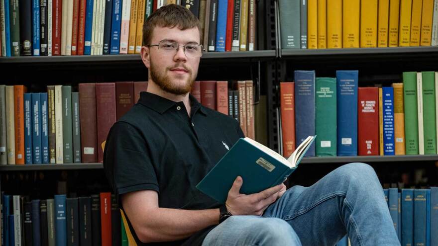 Noah Clark sits in a chair with a book in the library.