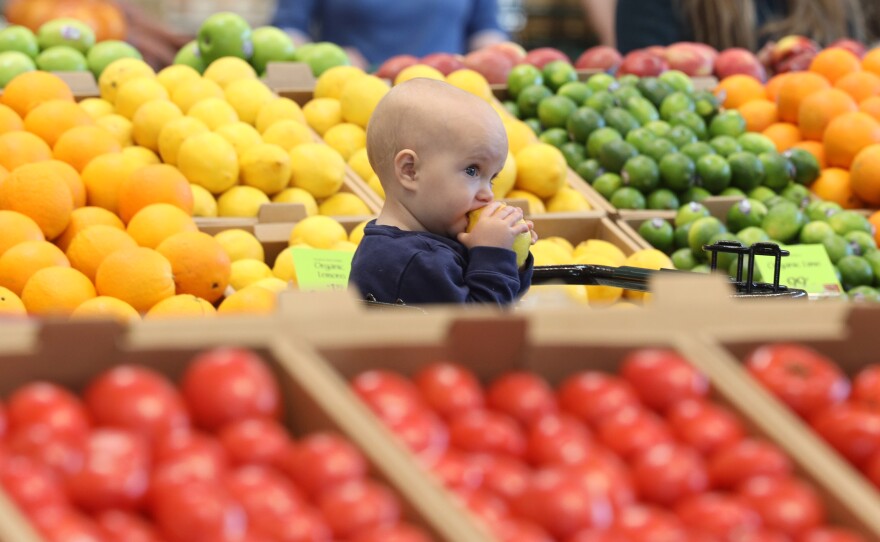 Ten-month-old Juni Riley enjoys a lemon while watching her mom, Lillian Riley, shop for fruit during the opening of the Whole Foods in Brighton on Wednesday, April 12, 2023.