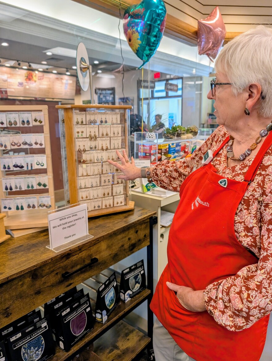 A woman points to an earring stand in a gift shop.