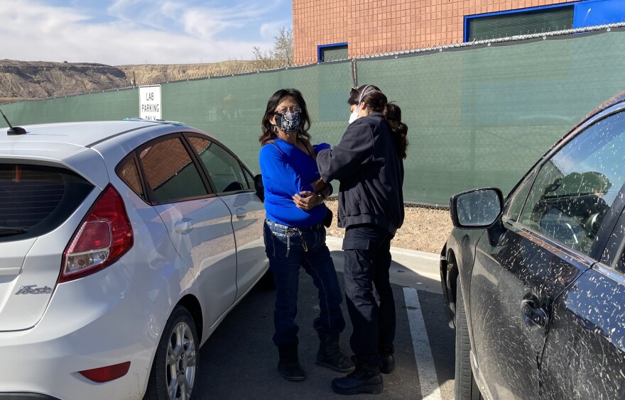 A woman in blue shirt gets a shot from a nurse wearing a navy jacket and pants. 
