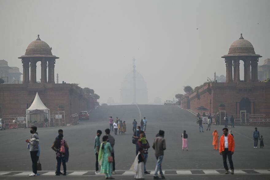 People stand on a street with two large temple-like structures, against a smoggy gray sky.