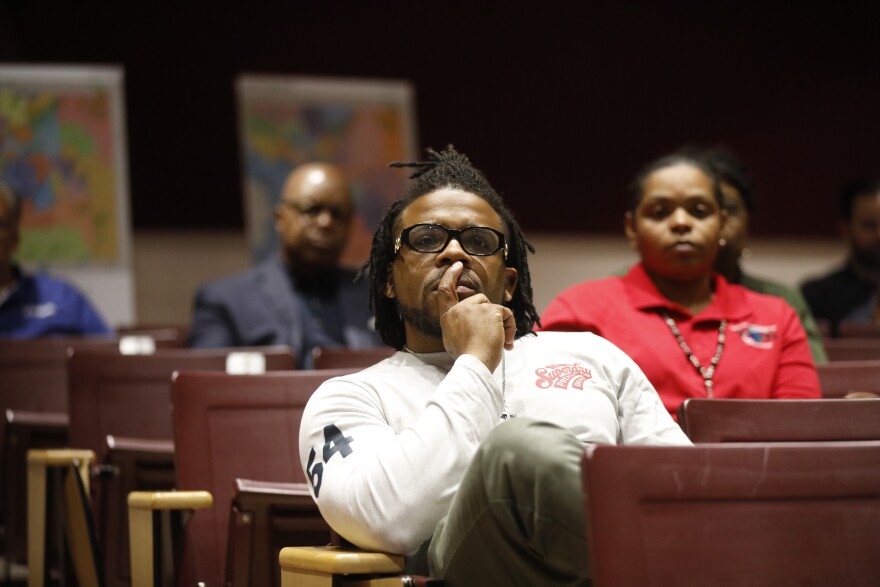 A man sits in a podium with his leg on the chair in front of him as he and other members of the community hear about school redistricting plans for Hillsborough County. 