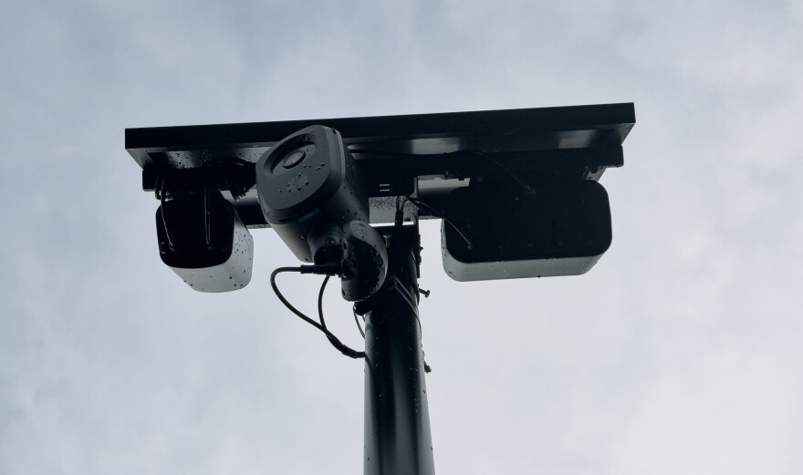 A Flock camera with a solar panel sits on a pole.