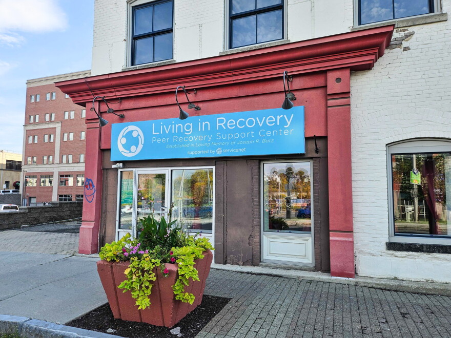 The storefront of Living in Recovery Peer Recovery Support Center in Pittsfield, Massachusetts. A blue sign with the center's name on it hangs above a brick facade.