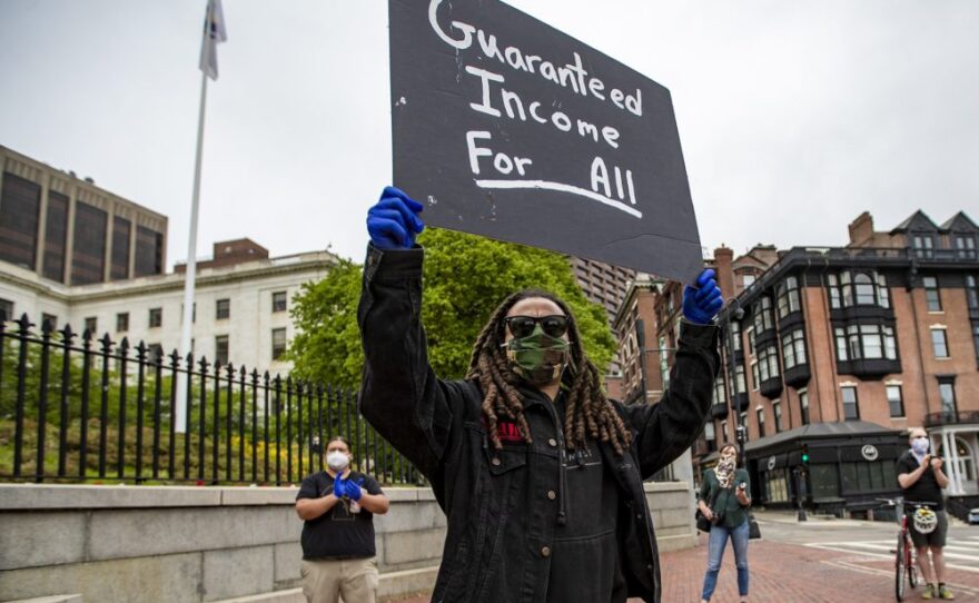 Armani White of the Black Boston COVID-19 coalition holds up a sign protesting in front of the Massachusetts Statehouse for the black and Latino people who have died of COVID-19.