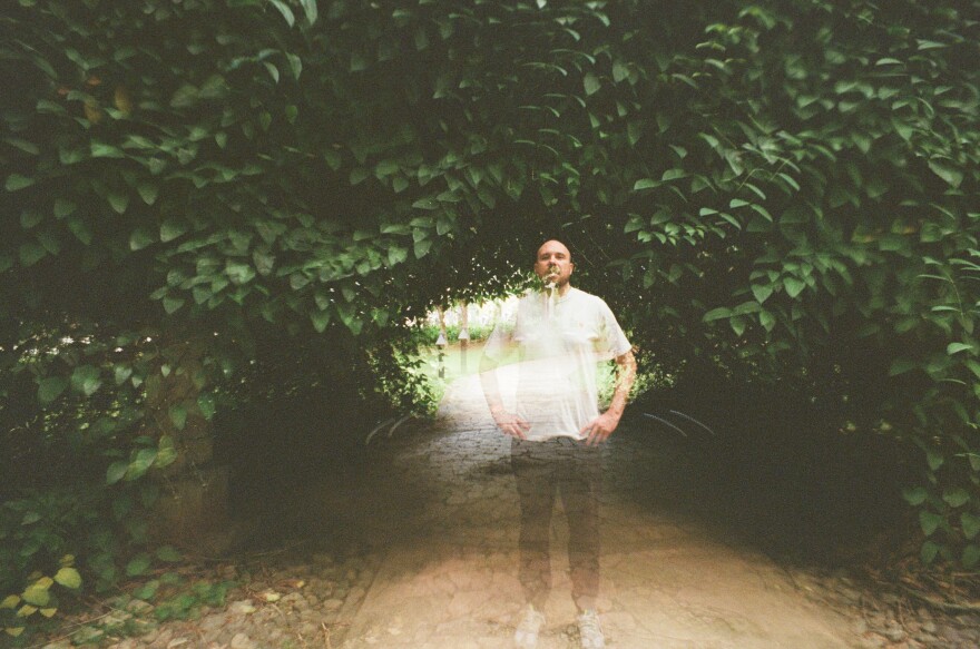 Lazerbeak is standing a little right of the center of the photograph. He is slightly transparent. The background is a green foliage tunnel.