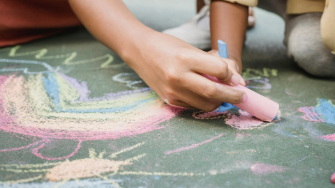 Close-up of two people drawing colorful chalk art on the pavement.
