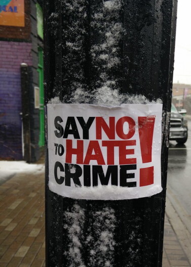 A sign attached to a black pole says "say no to hate crime" in large black and red letters on a white background.