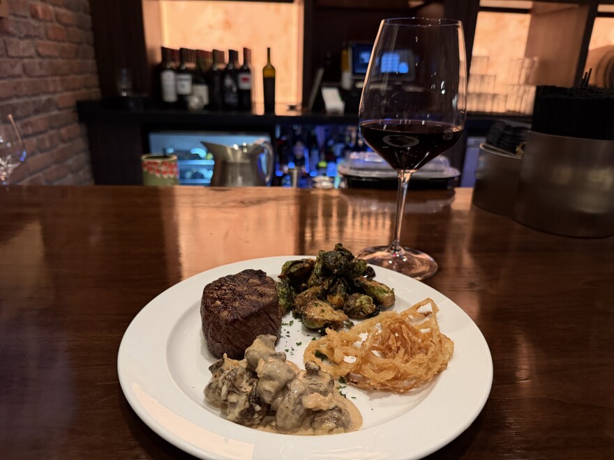 A seared filet mignon is served with roasted Brussels sprouts, crispy onion straws and a creamy mushroom side at the newly opened Harry’s Steak House in West Fargo, paired with a glass of red wine.