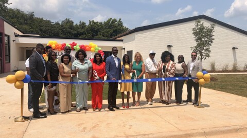 State, local and federal leaders stand behind a blue ribbon, ready to cut it marking the opening of a new early learning center in Birmingham's Titusville community.