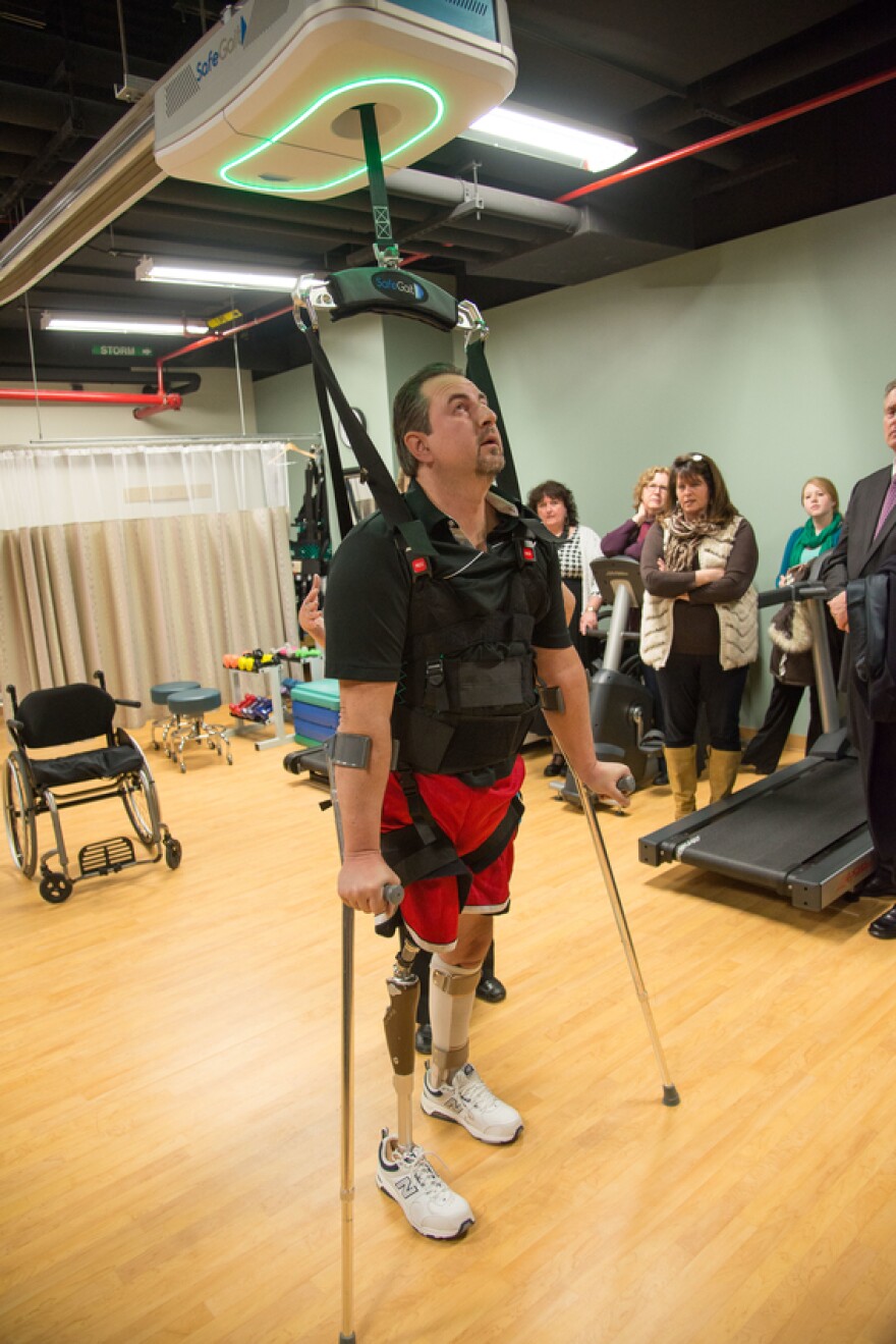 Landers walks on crutches while hooked up to the SafeGait.