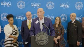 A white man in a blue blazer talks at a podium