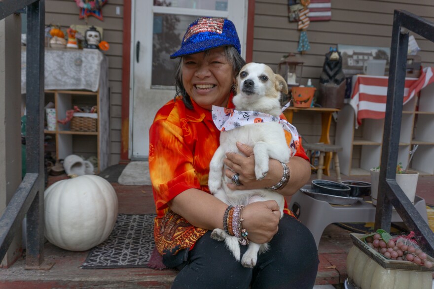 A woman in a red shirt sits on her porch and holds a small dog.