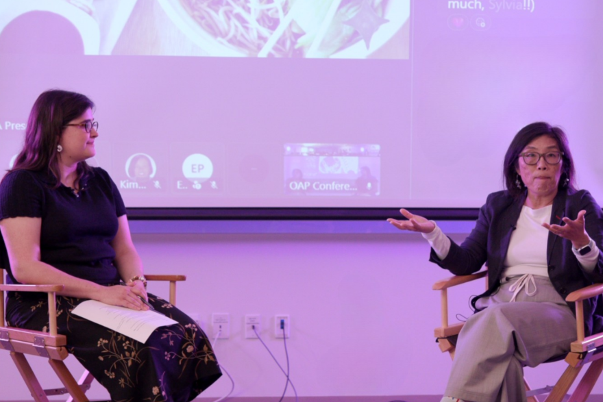 Miranda Suarez (left) and June Chow (right) sit in two directors chairs in a converence room, facing each other