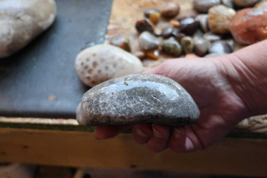 A man's hand holds a light gray rock with a slight circular pattern