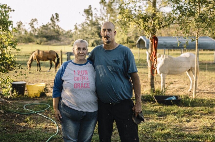 Susan Koppelman, 52, and Keith Koppelman, 49, stand for a portrait at a rural property outside Marianna, Fla., where they have been staying since being evicted from their trailer home after last year's hurricane. The landowners allow the couple to live in the storm-damaged house rent-free in exchange for help with the horses.