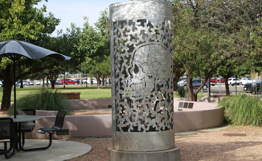 A large metal cylindrical lantern beside a picnic table in the courtyard, depicting the profile of a human skull.