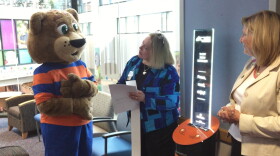 Akron Summit County Public Library mascot "Paws" displays the first story from the new dispenser at Akron Children's Hospital to hospital President Grace Wakulchik (right) and library Director Pam Hickson-Stevenson.
