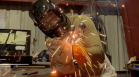 Sparks flying as a man with a welding mask and gloves welds a piece of metal art
